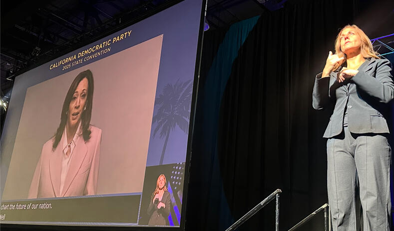 Interpreting for Kamala Kamala Harris on projected on large screen with interpreter in the corner