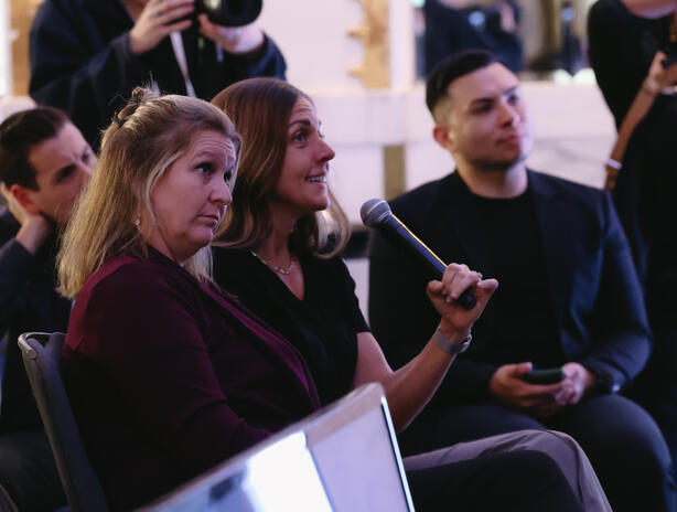 Platform Voice Interpreting Amber sitting in an audience holding a mic, looking toward stage.