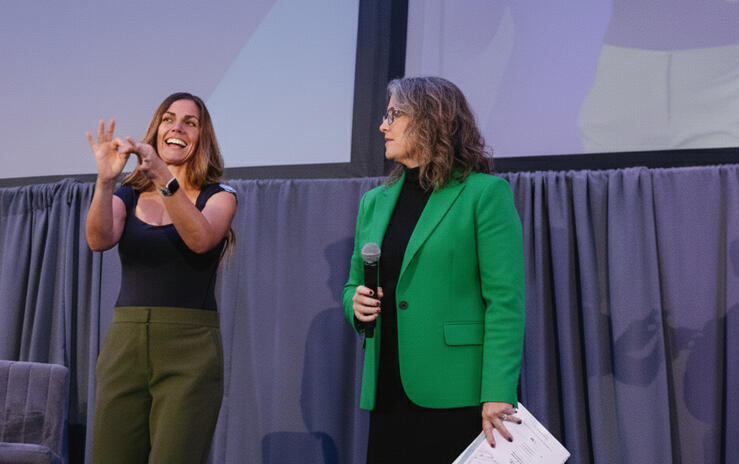 summit presentation interpreter on stage next to a hearing presenter, signing the word connect.